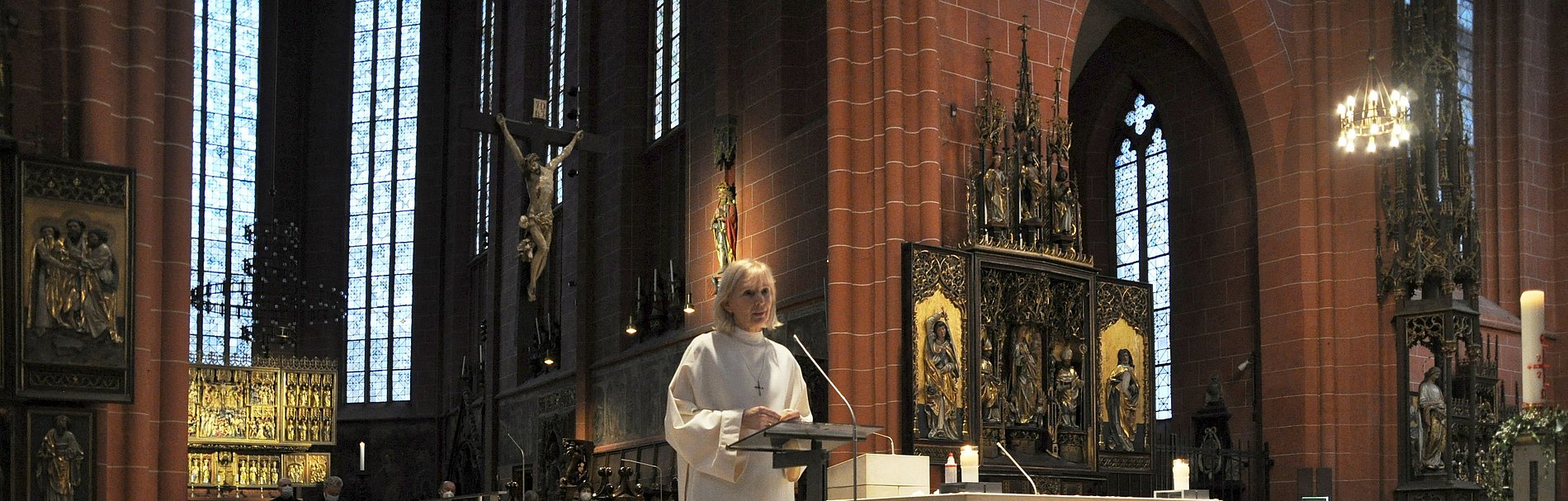 Eine Frau steht im liturgischen Gewand in einer Kirche. Ringsherum stehen unzählige Gedenkkarten für Corona-Verstorbene.