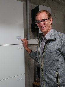 Stefan Römmele zeigt mit der Hand auf den Wärmespeicher im Technik-Raum des Gemeindezentrums.