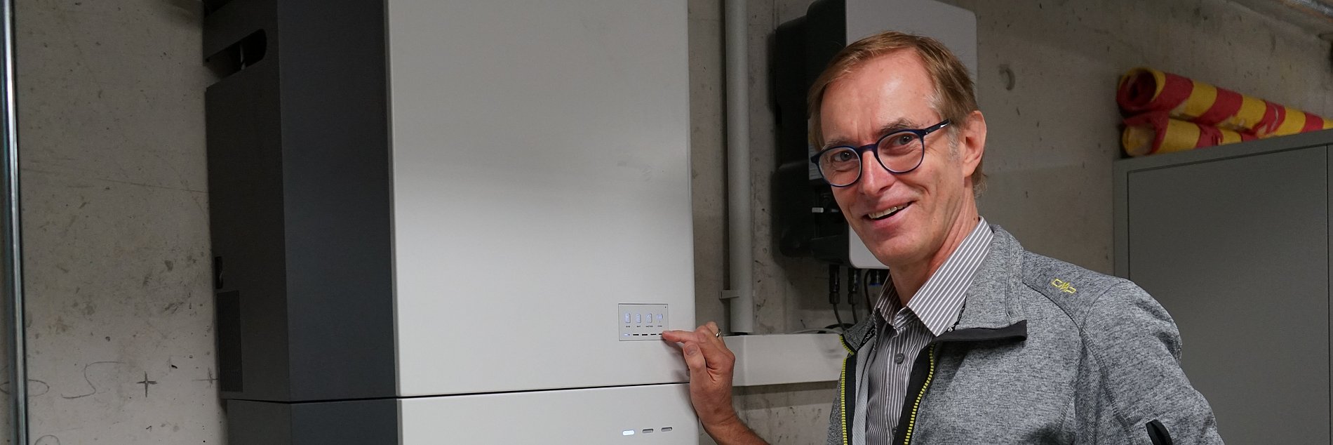 Stefan Römmele zeigt mit der Hand auf den Wärmespeicher im Technik-Raum des Gemeindezentrums.