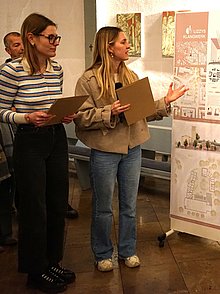 Die beiden Architekturstudentinnen stehen links neben ihren Planungsskizzen und erklären den Inhalt. Das Jurymitglied Peter Lesko steht rechts im Bild und hört zu.