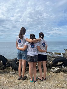 Drei junge Frauen stehen am Meer und umarmen sich