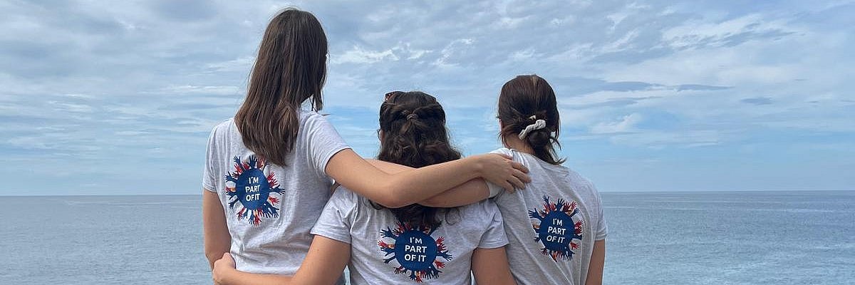 Drei junge Frauen stehen am Meer und umarmen sich